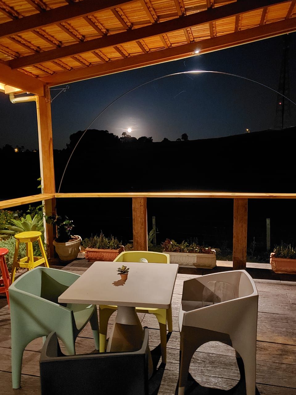 Deck noturno com mesa, cadeiras coloridas e lua ao fundo