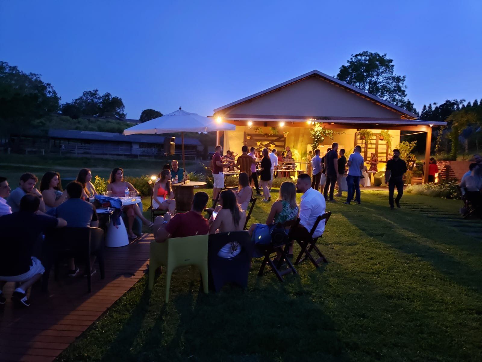 Pôr do sol com convidados sentados no deck e pavilhão iluminado